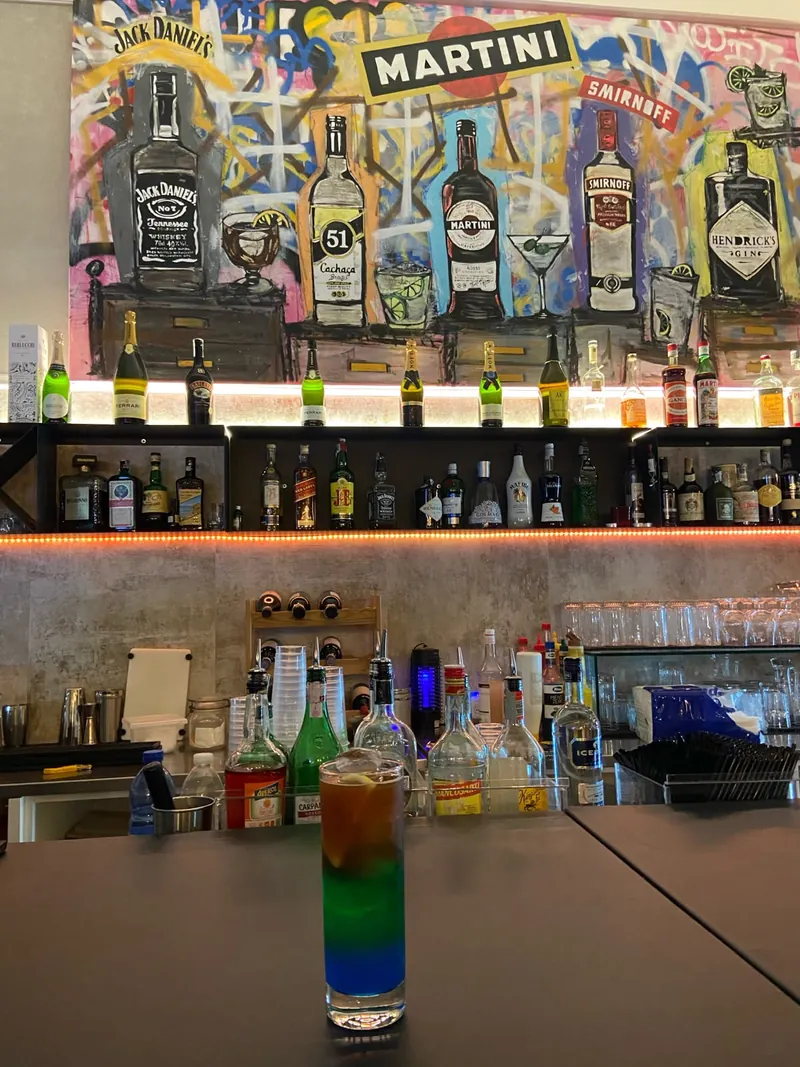Un cocktail a strati sul bancone, davanti alle bottiglie e al murale con Jack Daniel's, Martini e Smirnoff dipinti