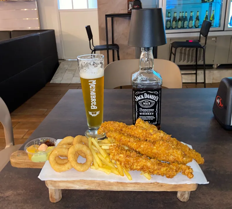 Tagliere con chicken tenders, anelli di cipolla e patatine, accanto a una birra Menabrea